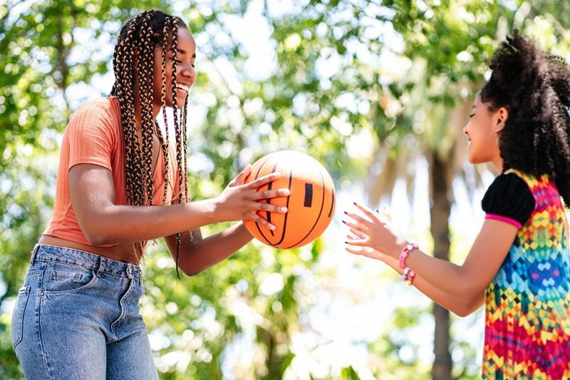 Little girl and her mother enjoying while playing basketball at the park